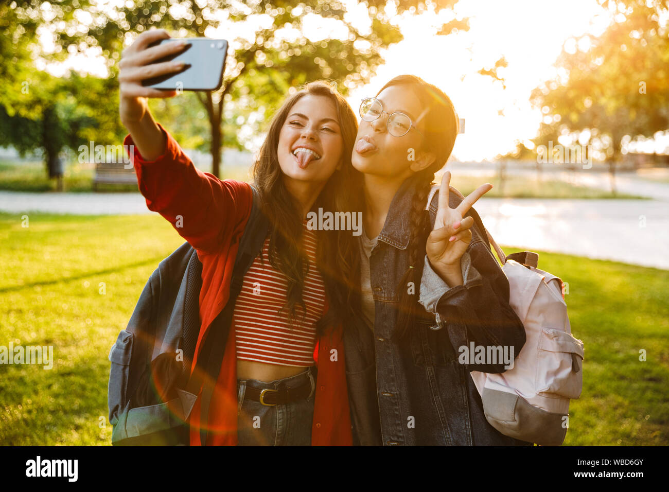Image de deux funny girls en langues sortir prendre la photo sur téléphone portable et selfies gesturing signe de paix en vous promenant dans Green Park Banque D'Images