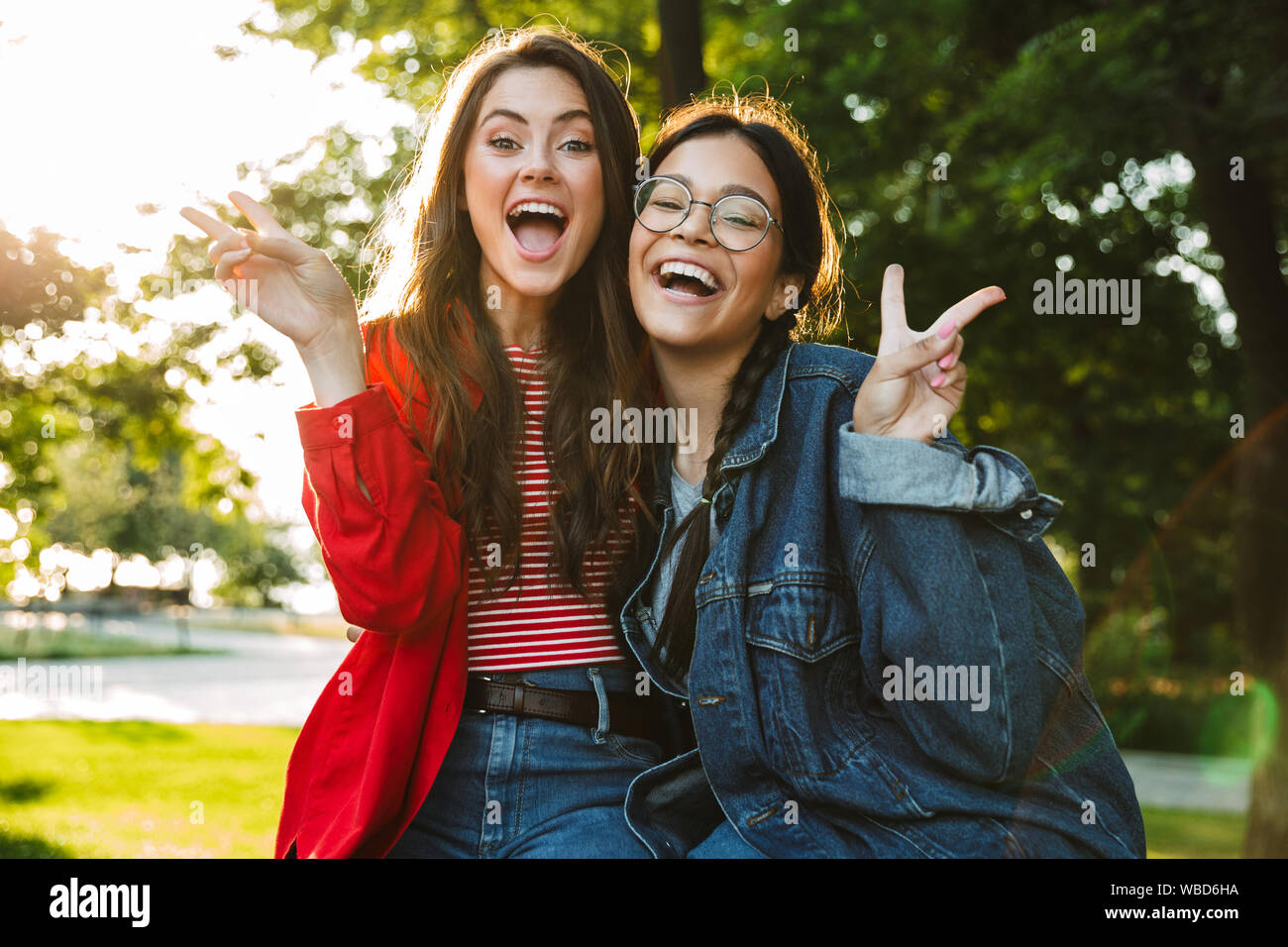 Image de deux élèves filles rire et chanter la paix gestes hugging tout en restant assis sur main courante en green park Banque D'Images