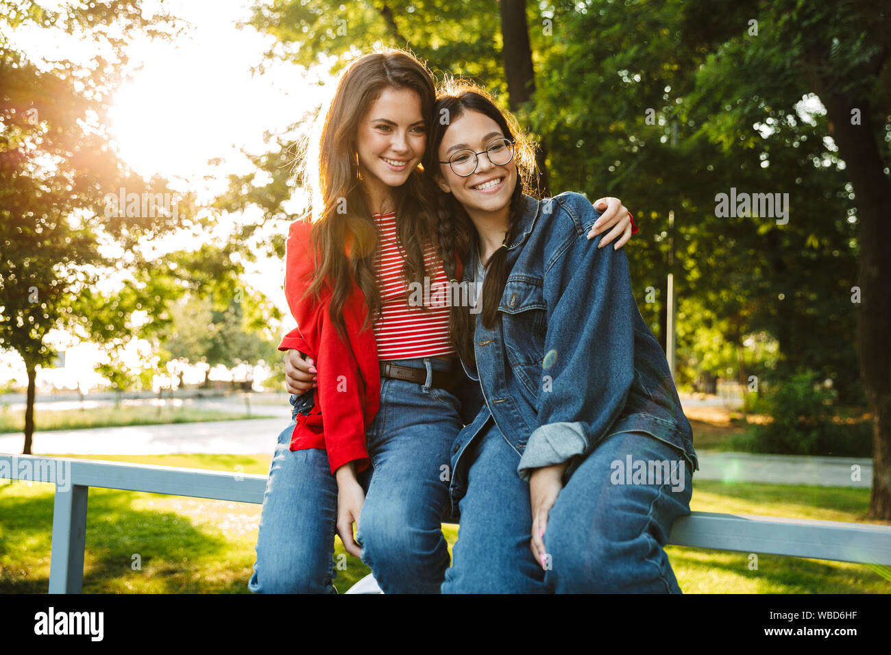 Image de deux élèves filles heureux souriant et serrant tout en restant assis sur main courante en green park Banque D'Images