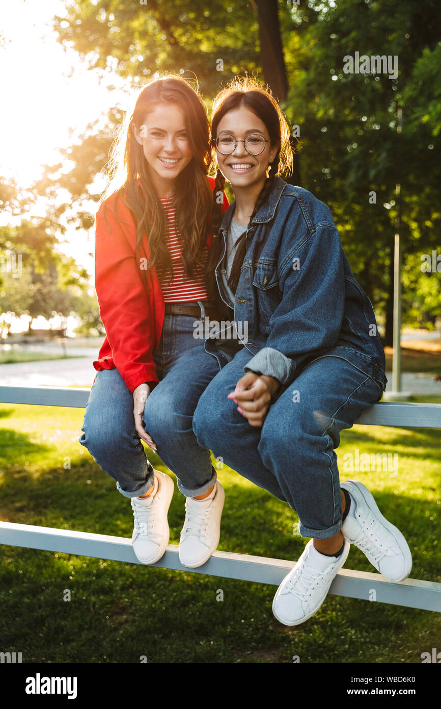 Image de deux filles attirantes students smiling et étreindre tout en restant assis sur main courante en green park Banque D'Images