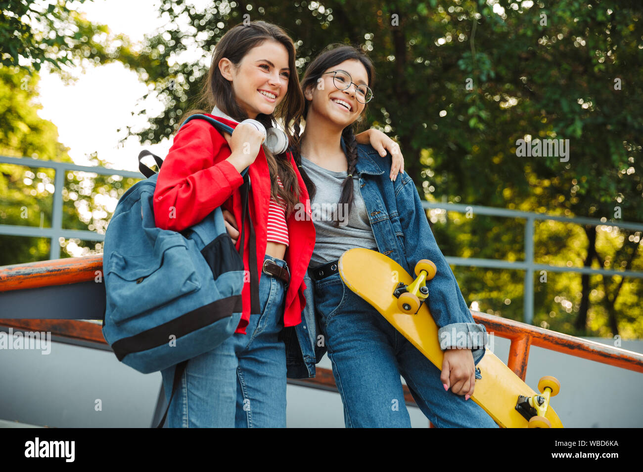 Image de deux heureux filles habillés en vêtements de denim en souriant et serrant ensemble tout en maintenant en skateboard skate park Banque D'Images