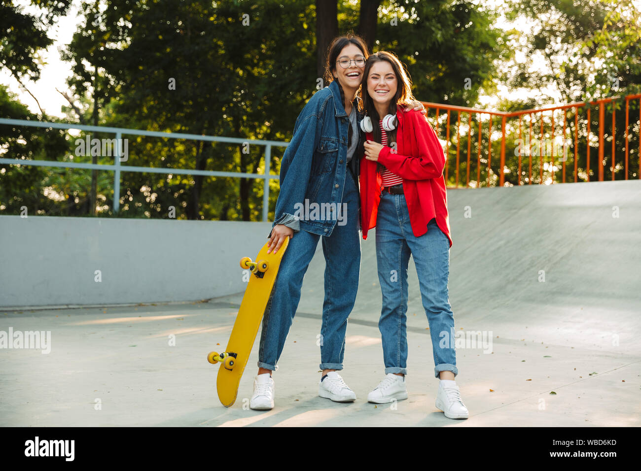 Image de deux filles brune vêtue de vêtements en denim de rire et s'étreindre ensemble tout en maintenant en skateboard skate park Banque D'Images