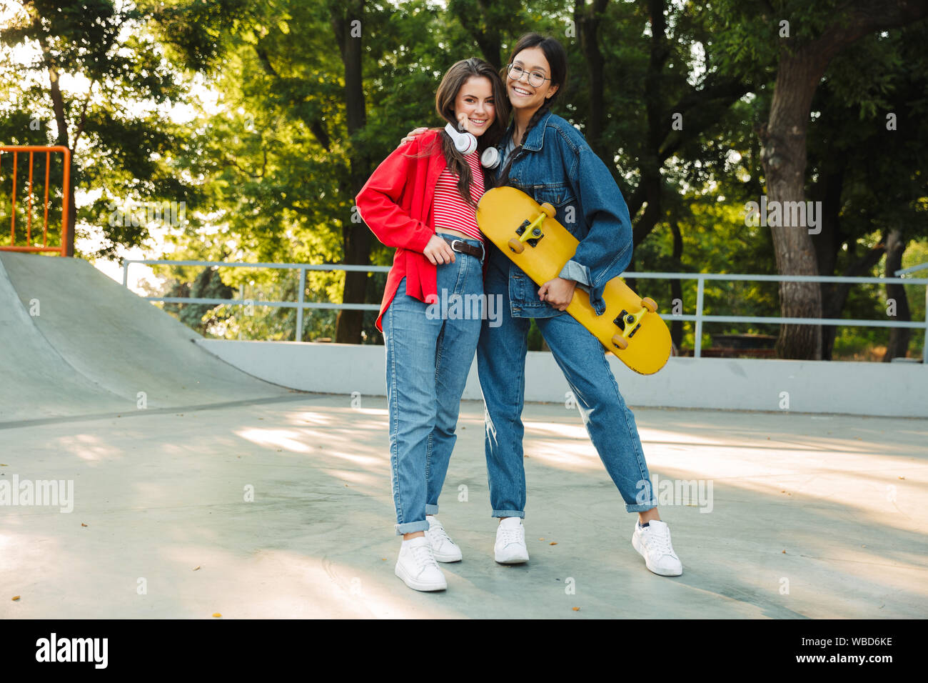 Image de deux professionnels des filles habillés en vêtements de denim en souriant et serrant ensemble tout en maintenant en skateboard skate park Banque D'Images