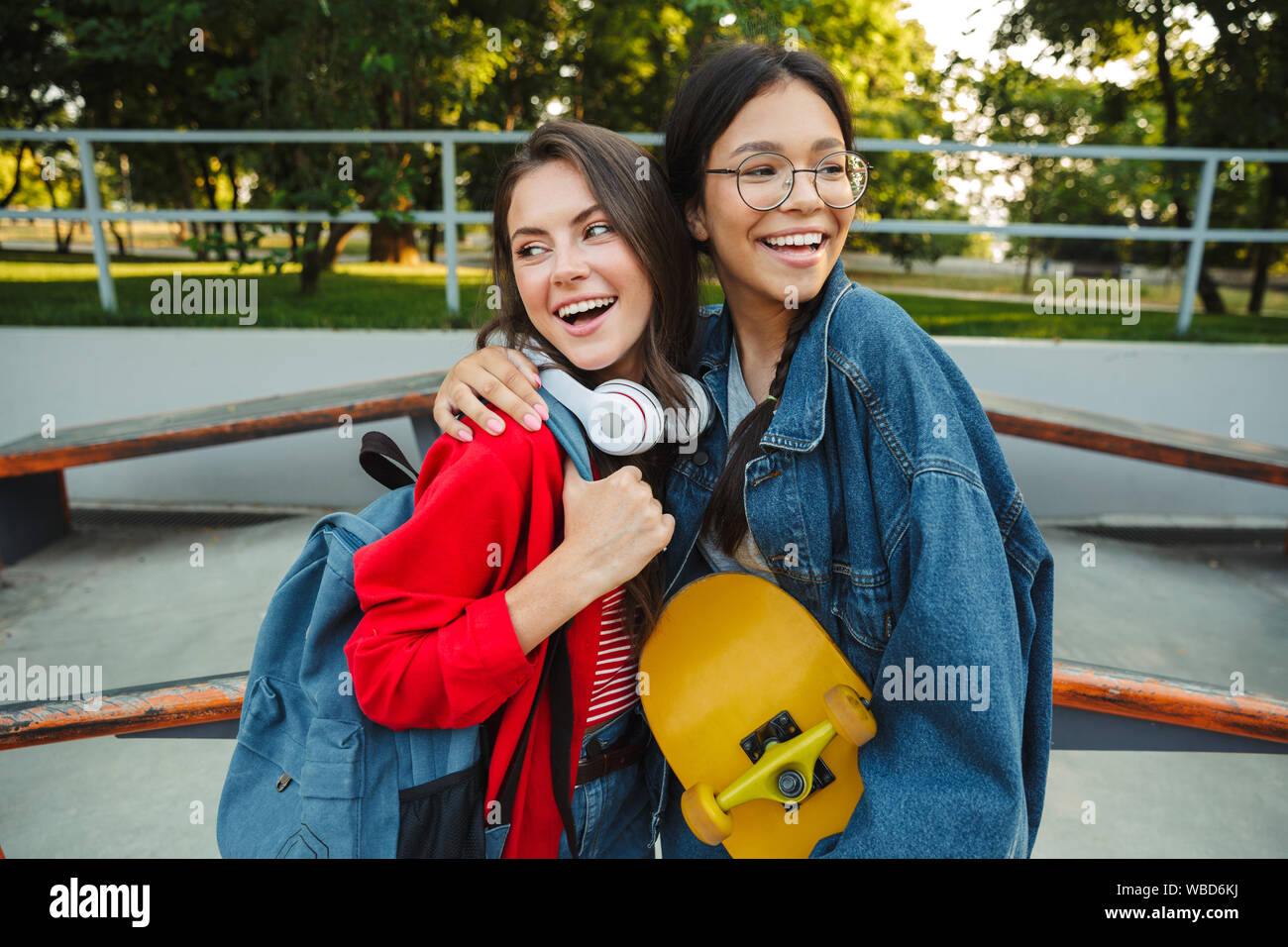 Image de deux filles attirantes habillés en vêtements de denim en souriant et serrant ensemble tout en maintenant en skateboard skate park Banque D'Images