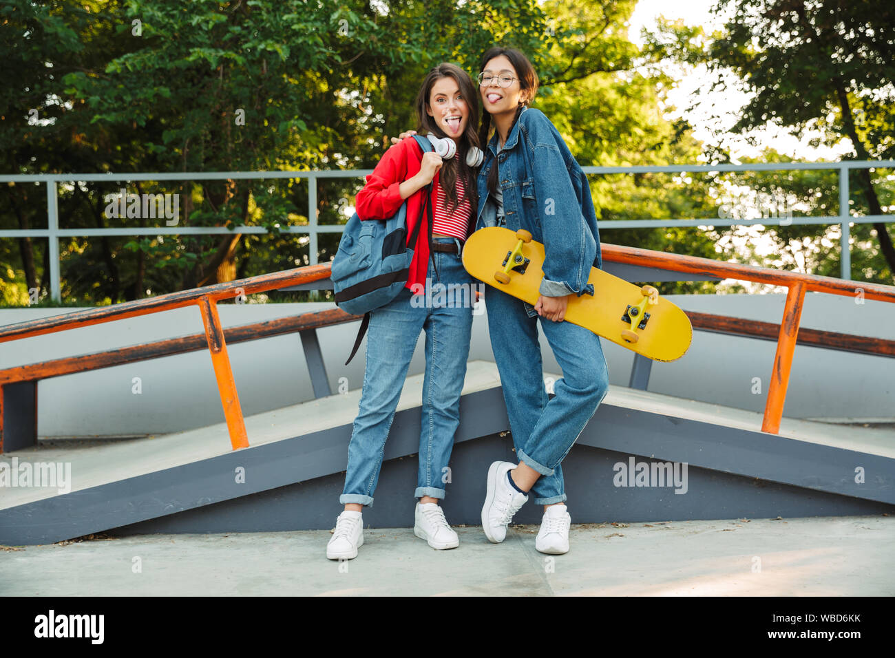 Image de deux filles de joie vêtu de vêtements en denim collage hors de leurs langues et s'étreindre en maintenant en skateboard skate park Banque D'Images