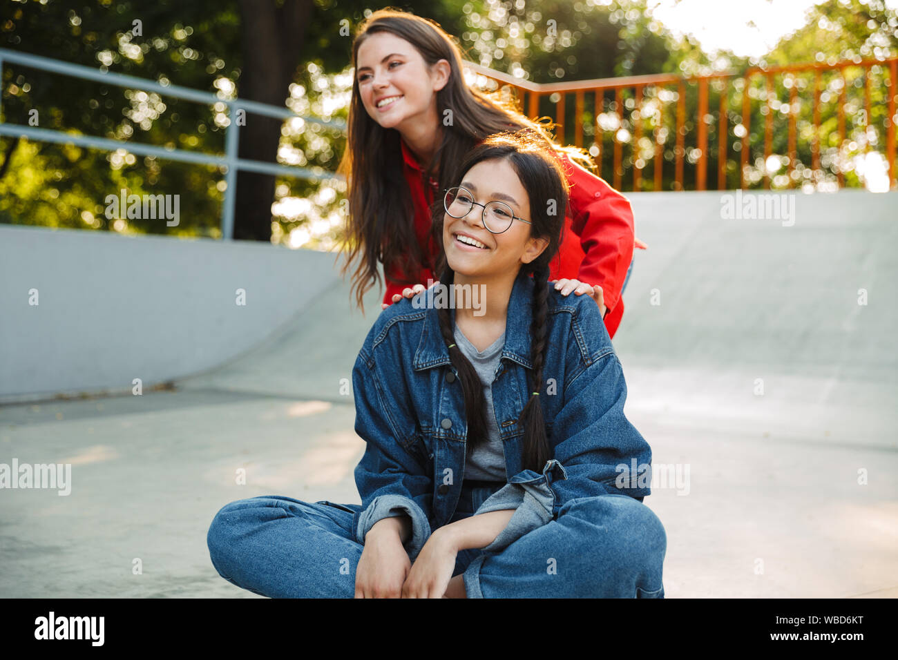 Image de deux jolies filles vêtus de vêtements en denim de rire et équitation skateboard ensemble dans skate park Banque D'Images