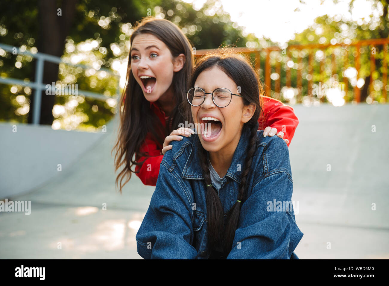 Image de deux filles ravi habillé en criant et porter denim skateboard équitation ensemble dans skate park Banque D'Images