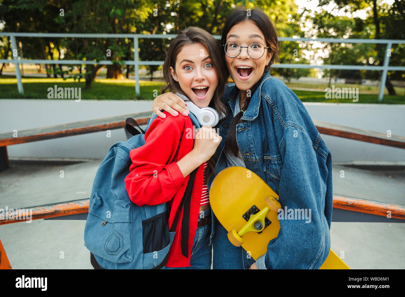 Image de deux excités filles habillés en vêtements de denim en souriant et serrant ensemble tout en maintenant en skateboard skate park Banque D'Images