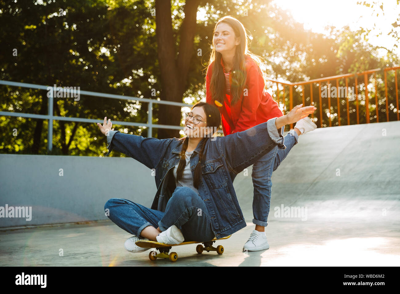 Image de deux professionnels des filles habillés en vêtements de denim et de l'équitation rire ensemble en skateboard skate park Banque D'Images