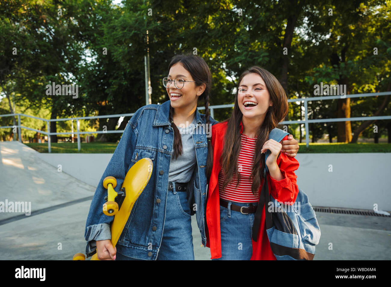 Image de deux adorables filles habillés en vêtements de denim en souriant et serrant ensemble tout en maintenant en skateboard skate park Banque D'Images