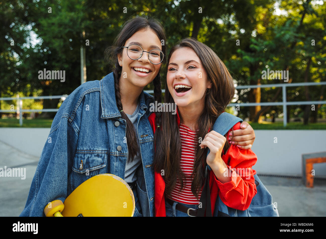 Image de deux jeunes filles de race blanche habillée de vêtements en denim de rire et s'étreindre ensemble tout en maintenant en skateboard skate park Banque D'Images