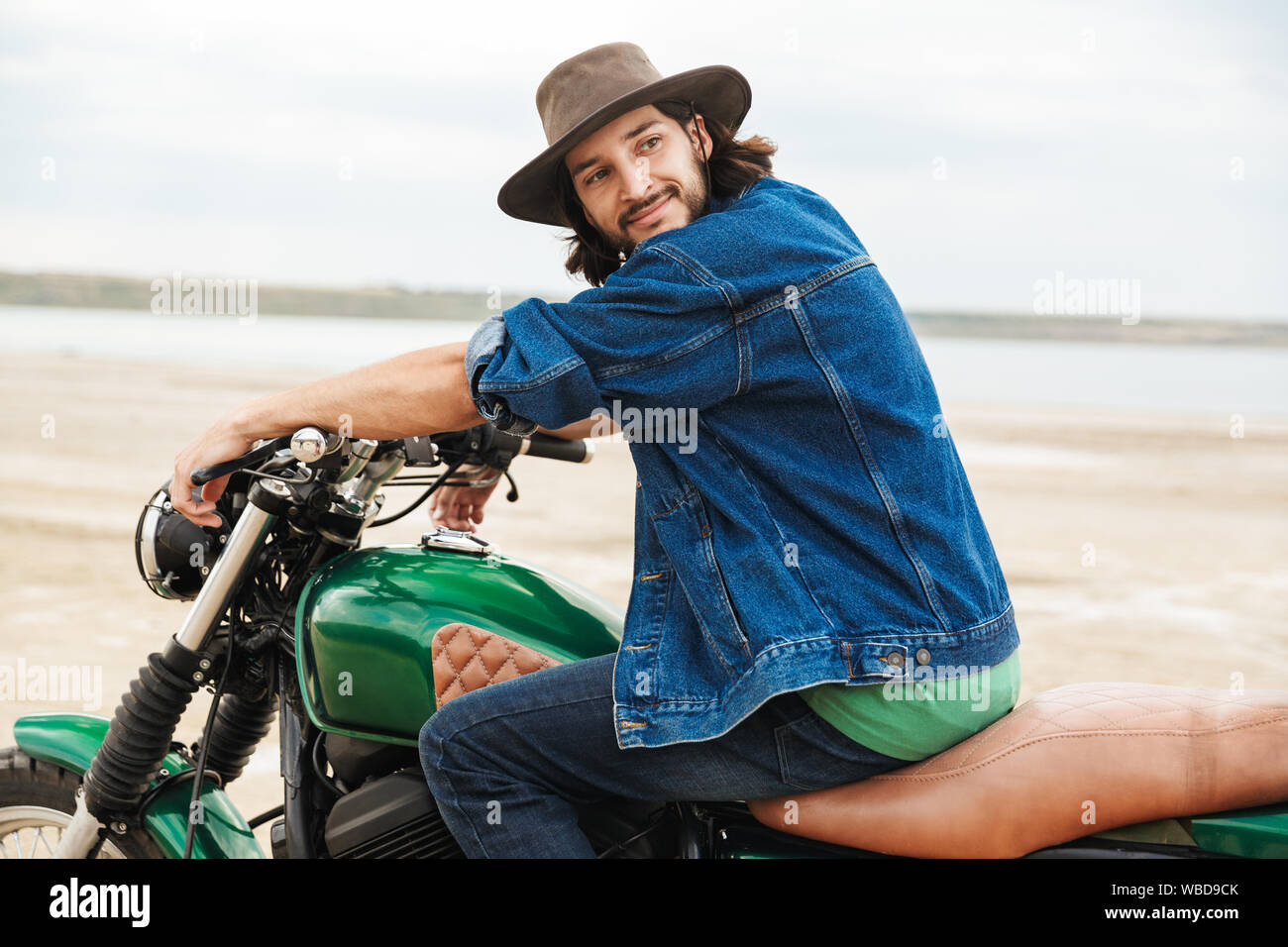 Vue latérale d'un beau jeune homme portant tenue décontractée assis sur une moto à la plage Banque D'Images