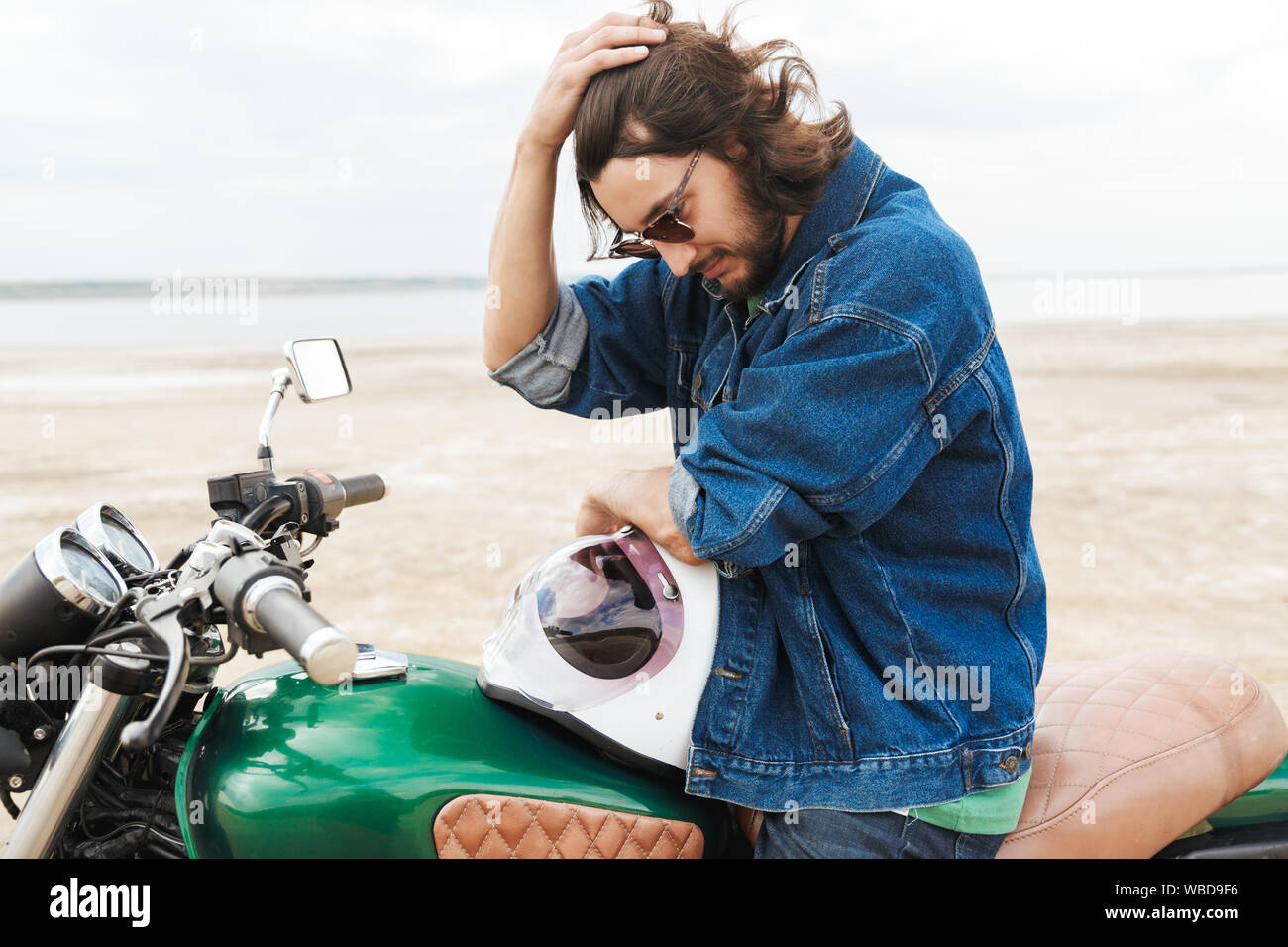 Beau jeune homme portant tenue décontractée assis sur une moto à la plage Banque D'Images