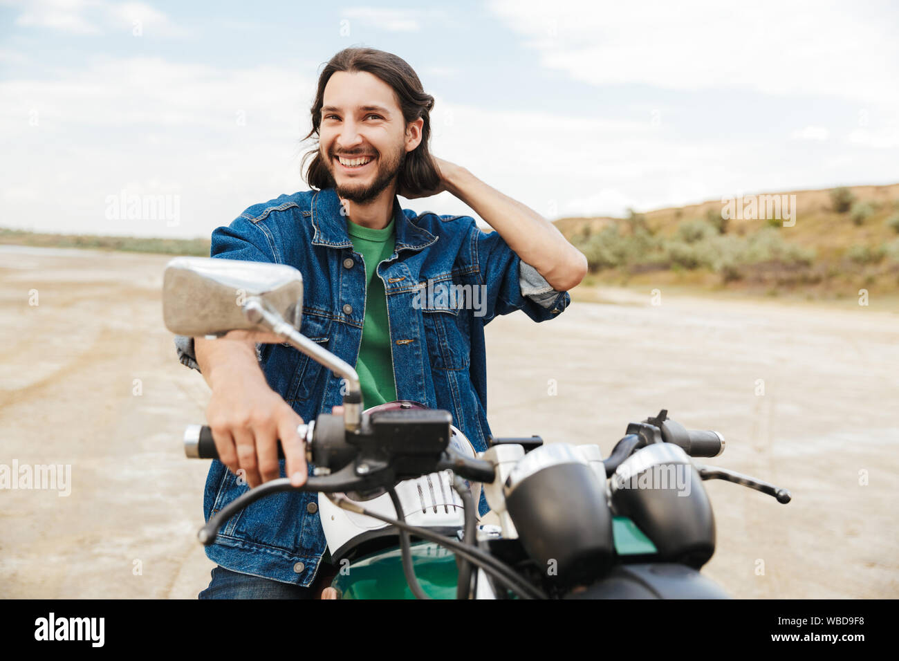 Handsome young man wearing tenue décontractée assis sur une moto à la plage Banque D'Images
