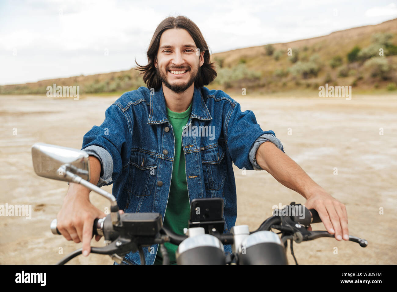 Close up d'un beau jeune homme portant tenue décontractée assis sur une moto à la plage Banque D'Images