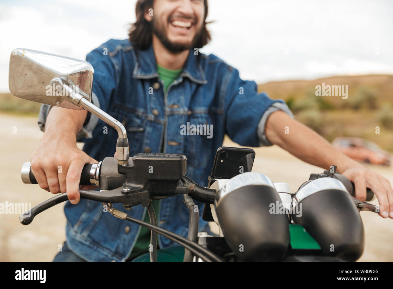 Portrait of a handsome smiling young man wearing tenue décontractée assis sur une moto à la plage Banque D'Images