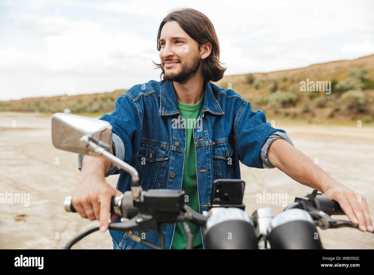 Close up d'un beau jeune homme portant tenue décontractée assis sur une moto à la plage Banque D'Images