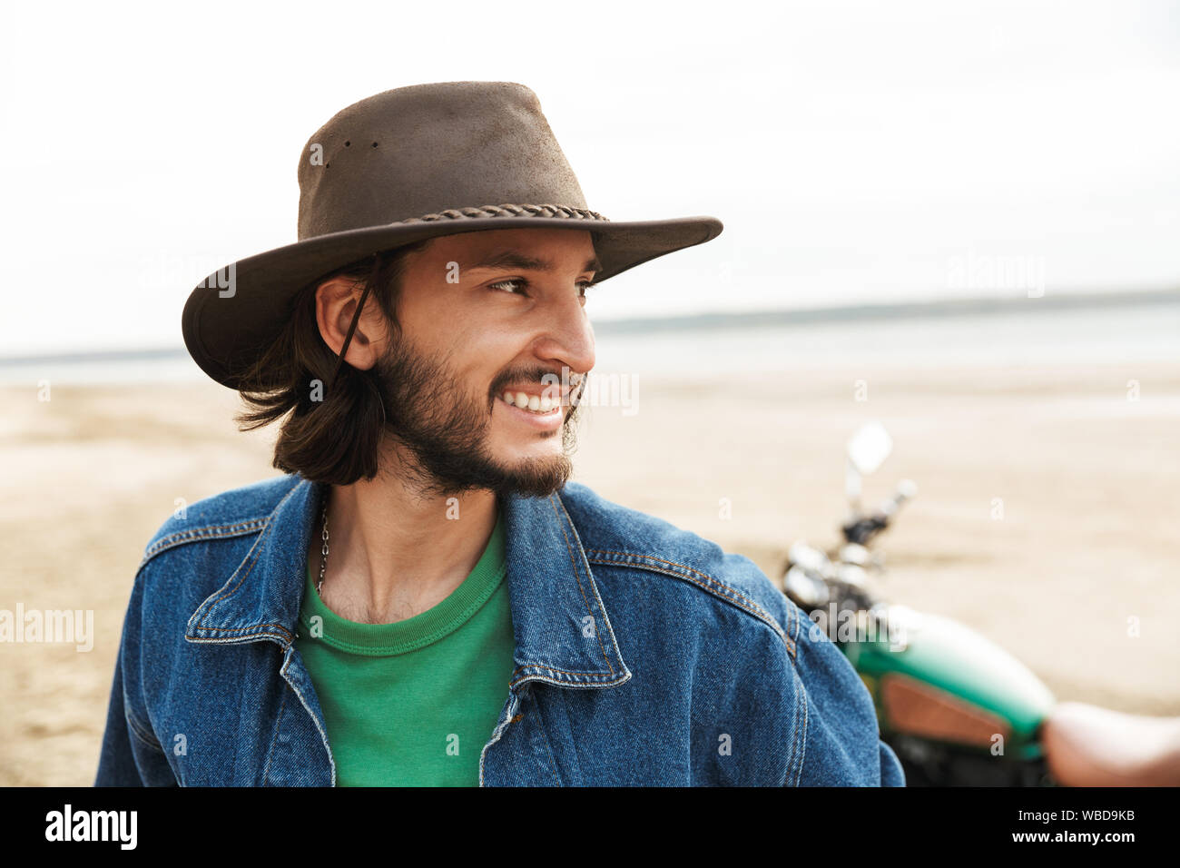 Close up of a handsome smiling young man wearing tenue décontractée debout à moto à la plage Banque D'Images