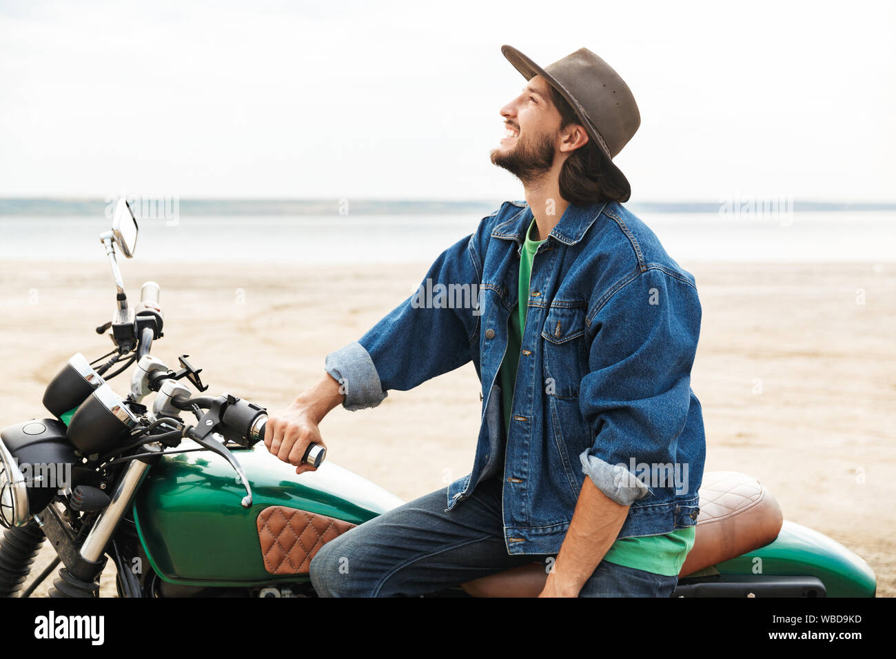 Beau jeune homme portant tenue décontractée assis sur une moto à la plage Banque D'Images