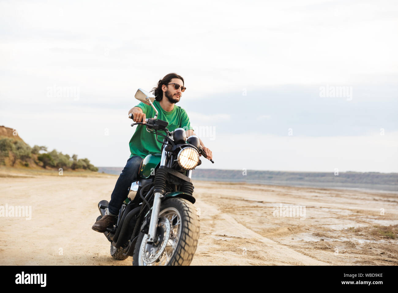 Beau jeune homme portant tenue décontractée circonscription une moto à la plage Banque D'Images