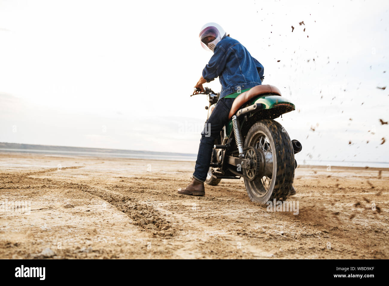 Vue arrière d'un jeune homme portant une tenue décontractée circonscription moto à la plage, le port d'un casque Banque D'Images