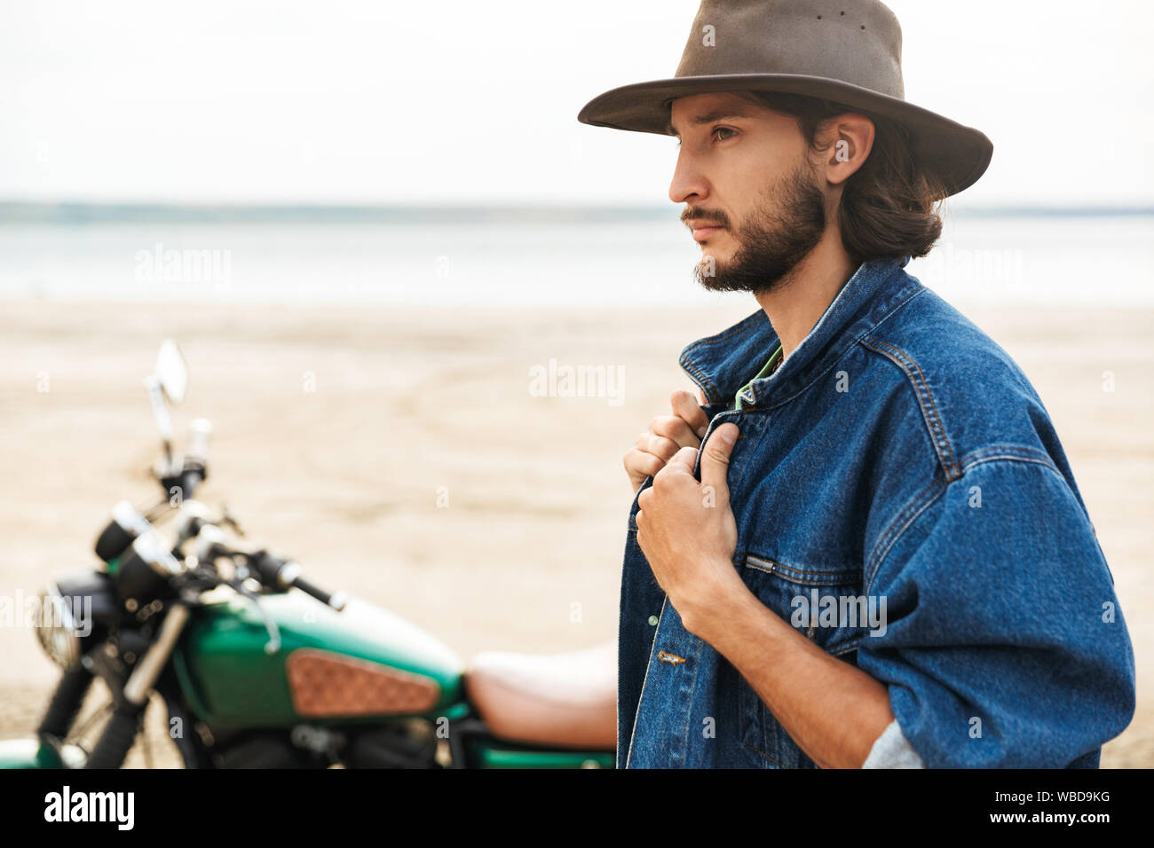 Close up d'un beau jeune homme portant tenue décontractée debout à moto à la plage Banque D'Images