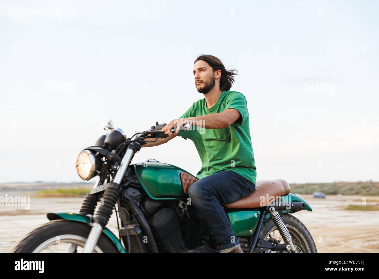 Vue latérale d'un beau jeune homme portant tenue décontractée circonscription une moto à la plage Banque D'Images