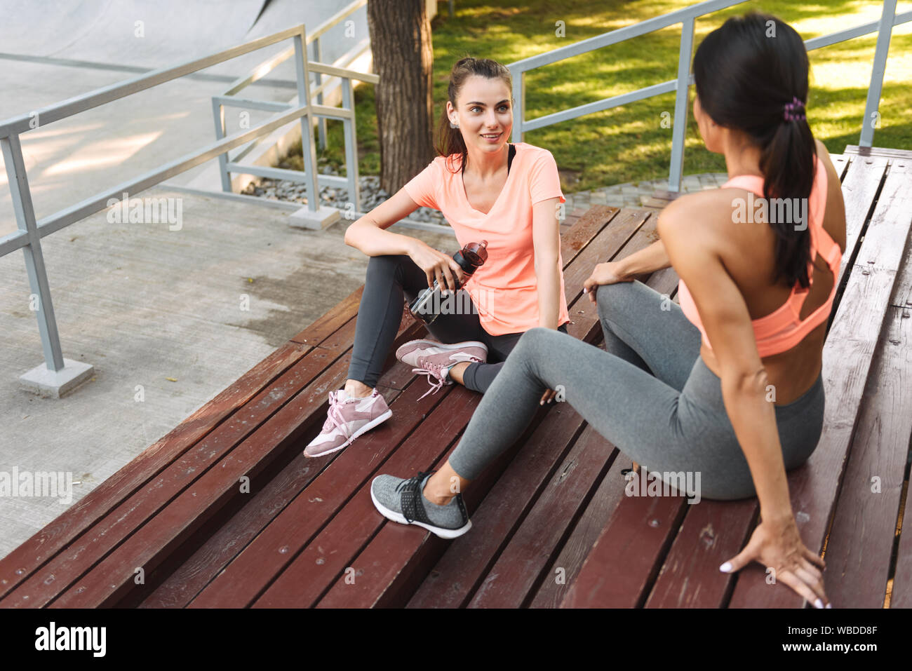 Image de jolies femmes en parlant de sport et de l'eau potable à partir de la bouteille tandis que assis sur un banc dans un terrain de sport Banque D'Images