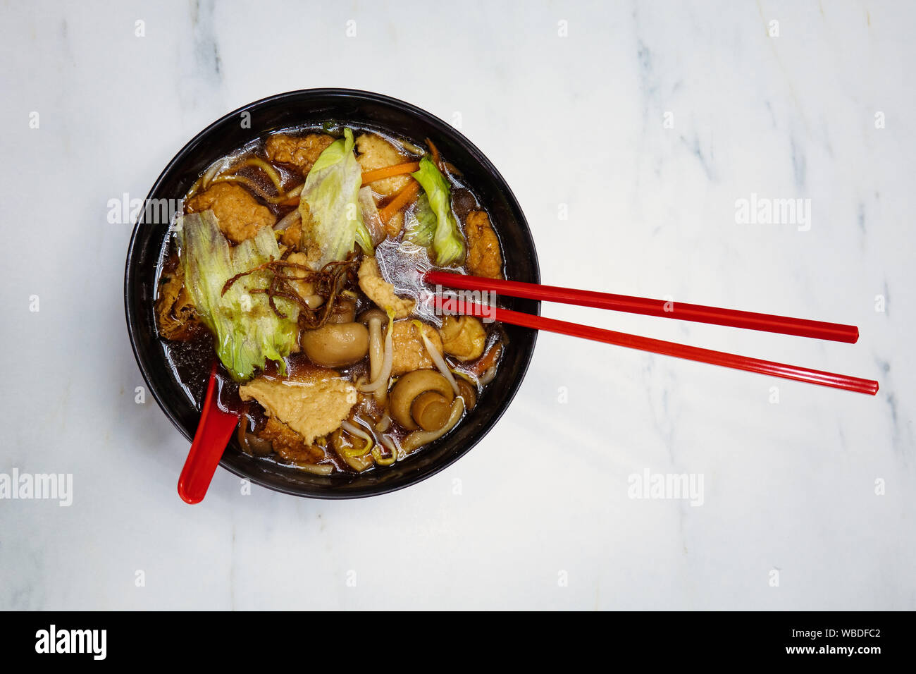 Un végétalien tofu aux champignons et nouilles asiatiques en soupe claire, servi dans un bol avec des baguettes noir rouge dans un restaurant à Singapour. Banque D'Images