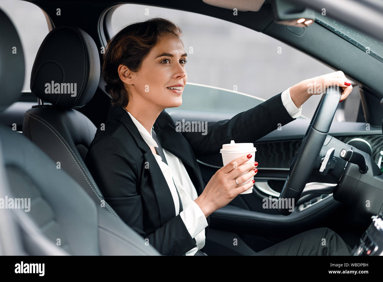 Businesswoman going à bureau dans sa voiture. Vue de côté de la pilote tenant un café. Banque D'Images