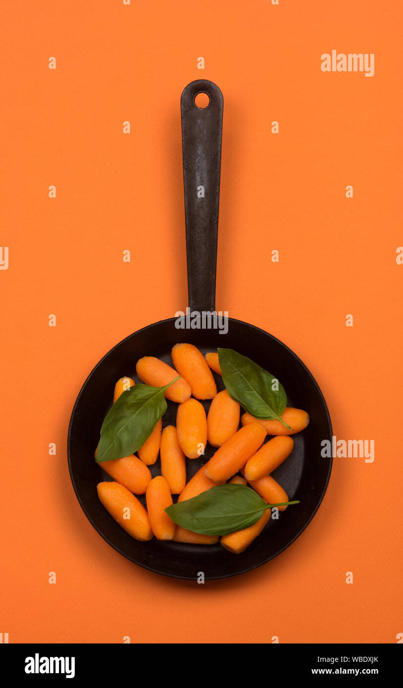Carotte bébé sur la poêle. Isolé sur orange. Banque D'Images