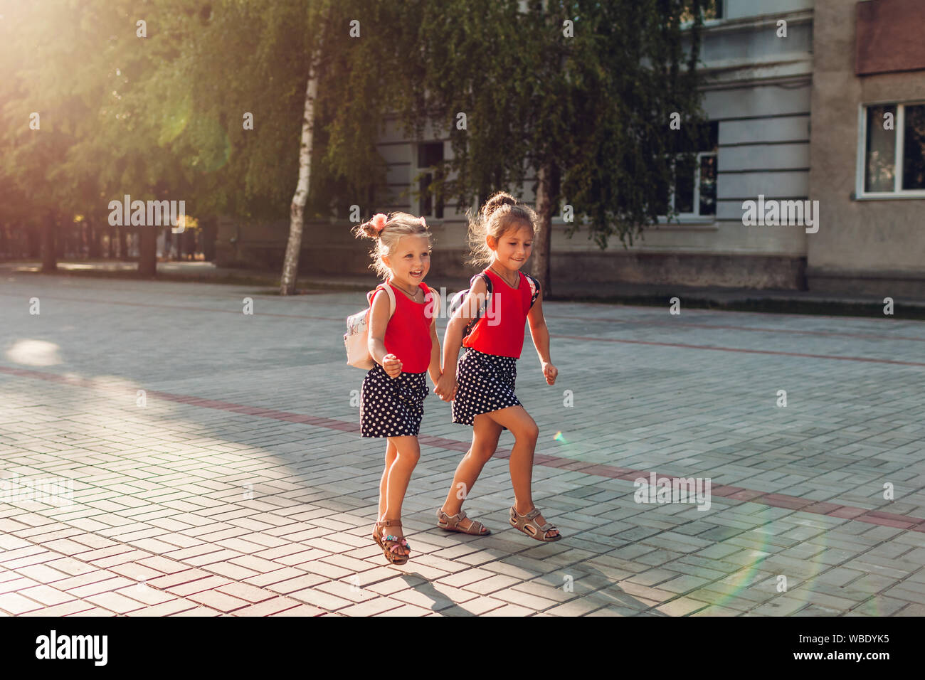 Heureux soeurs filles portant des sacs à dos et d'exécution. Les élèves s'amuser les enfants près de l'école. L'éducation. Retour à l'école Banque D'Images