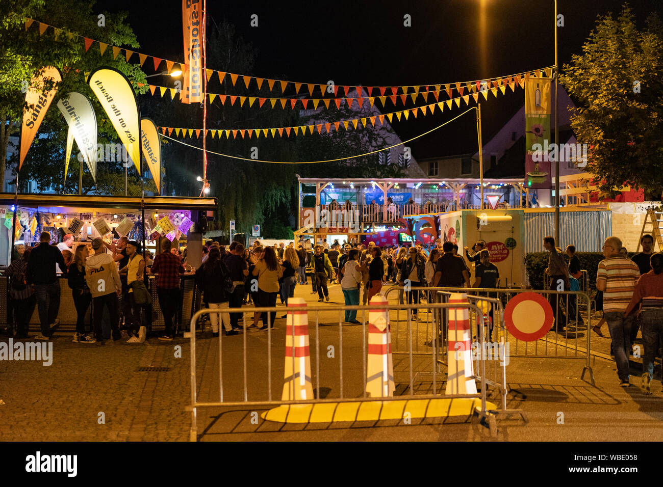 Stadtfest Brugg 24 août 2019. Photographie de rue. Hot-Shots-Bar dans la partie de la ville illuminée avec banderoles colorées de nombreuses personnes et de sécurité des bornes Banque D'Images