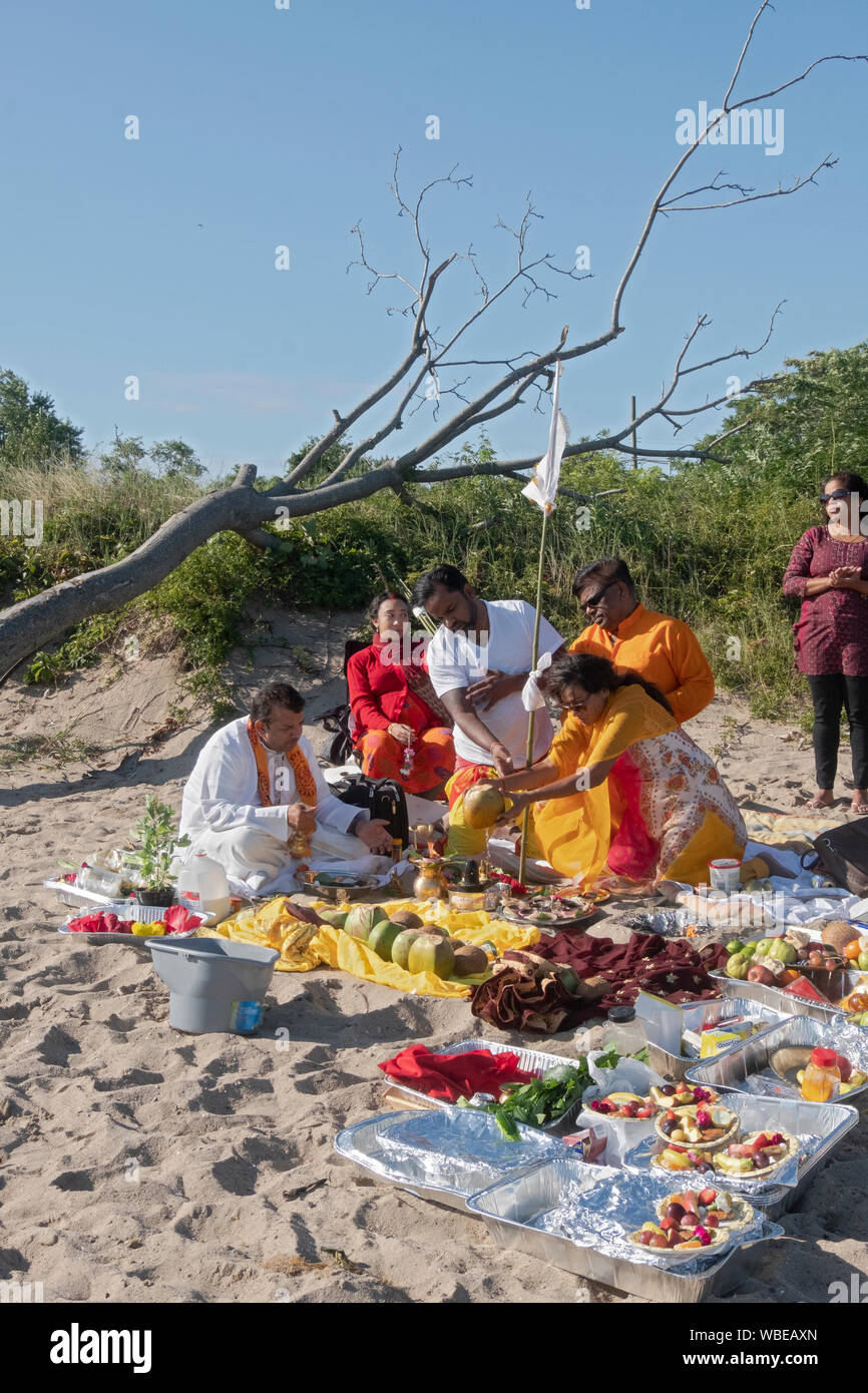 Une femme hindoue pieuse verse du lait de coco à une famille lors d'un service de prière en plein air sur une plage à Jamaica Bay dans le Queens, New York. Banque D'Images