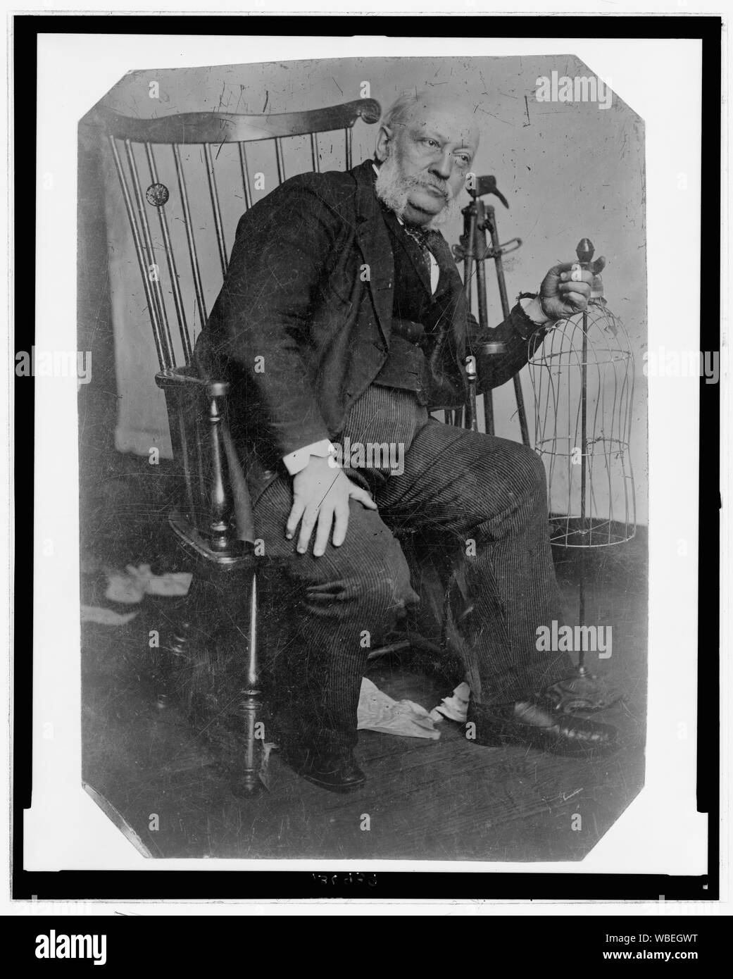 Portrait en pied d'un homme, assis sur une chaise, penché sur un côté de sa main gauche, reposant sur un châssis de vêtements( ?) Résumé/moyenne : 1 tirage photographique : ferrotype. Banque D'Images