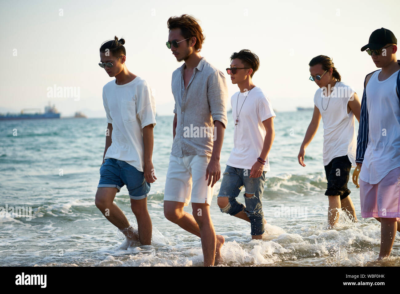 Groupe de cinq jeunes hommes asiatiques marcher dans l'eau de mer sur la plage Banque D'Images