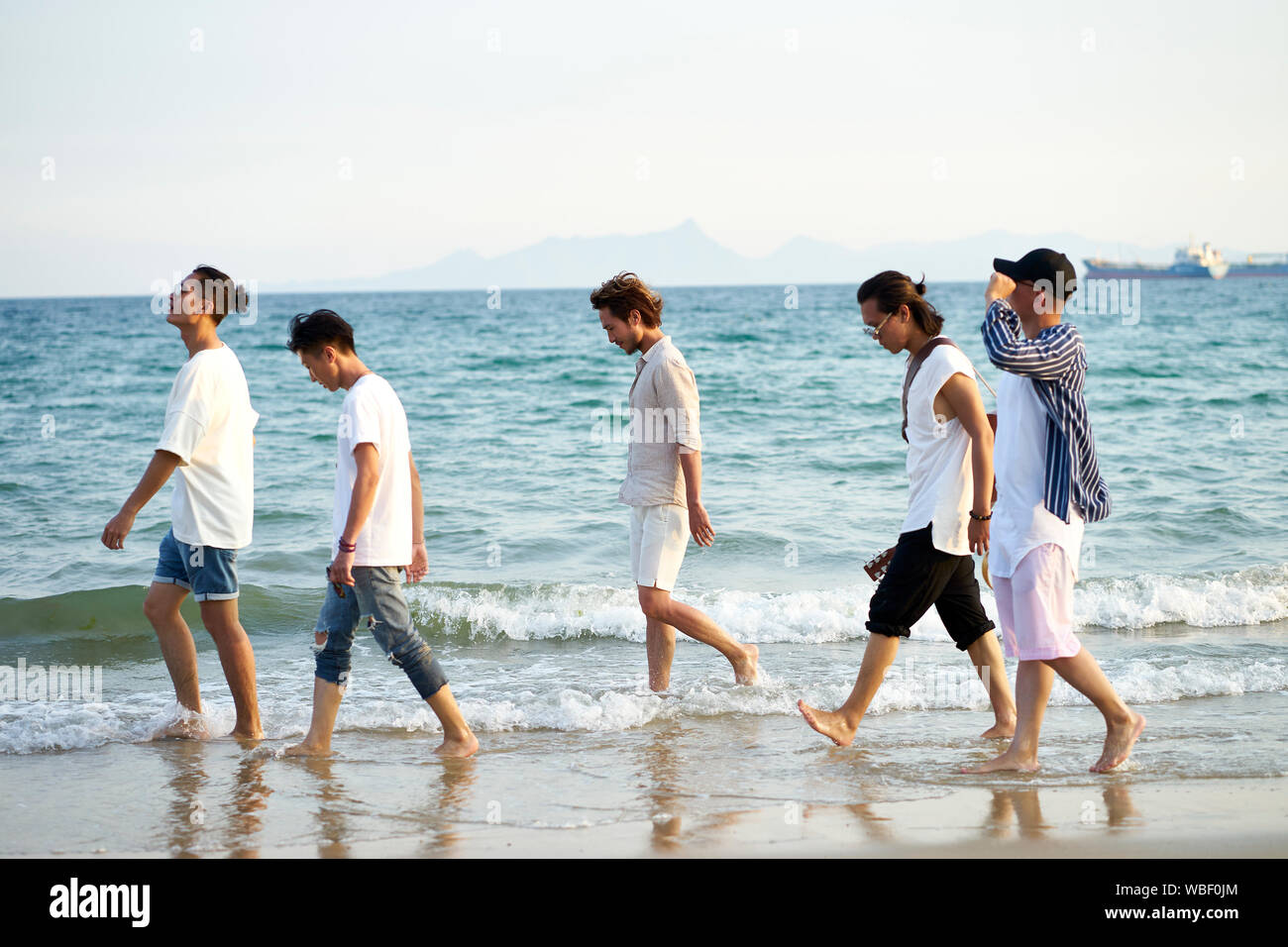 Groupe de cinq jeunes hommes asiatiques marcher dans l'eau de mer sur la plage Banque D'Images