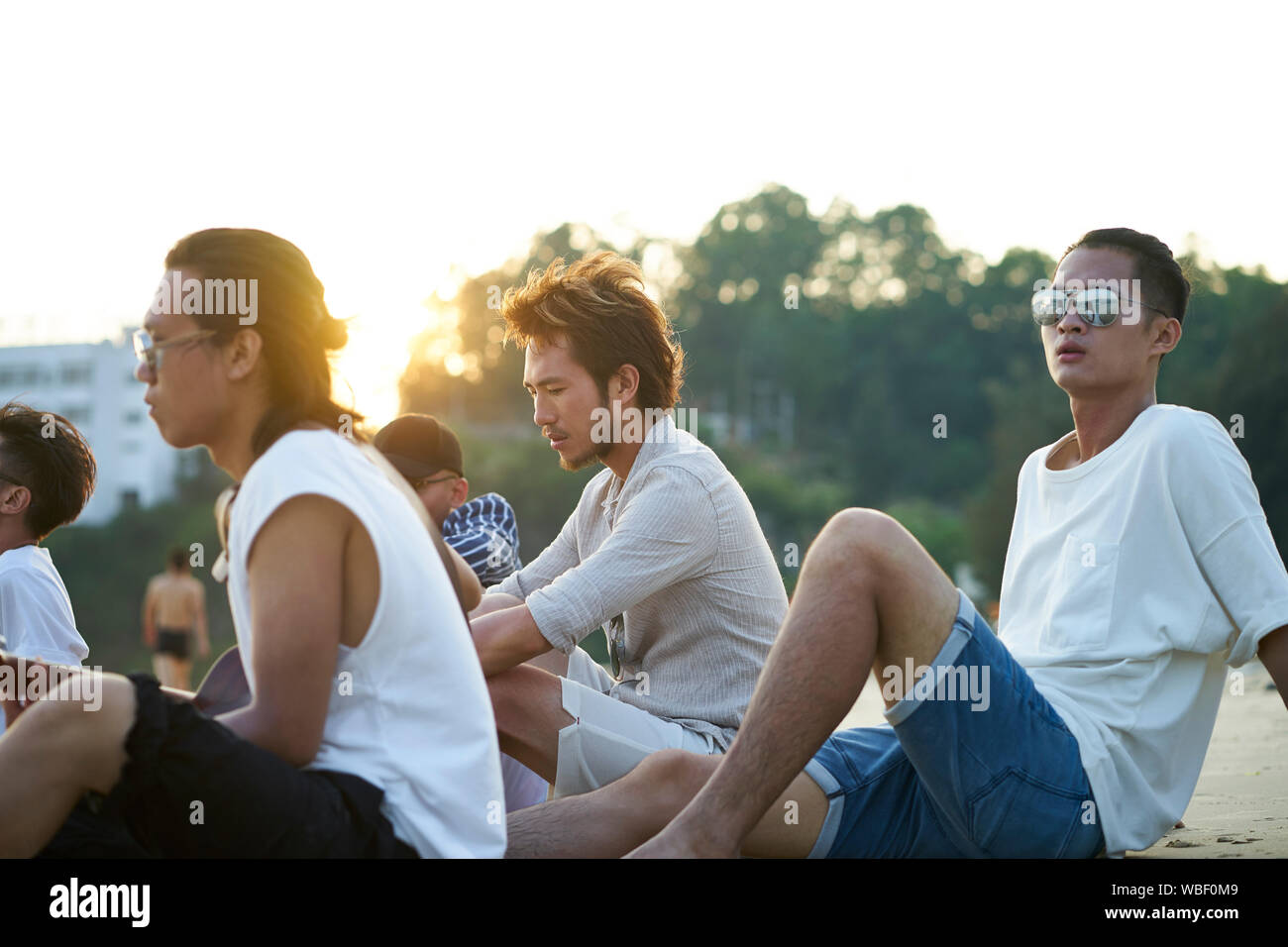 Groupe de cinq jeunes hommes asiatiques assis sur la plage de sable au crépuscule Banque D'Images