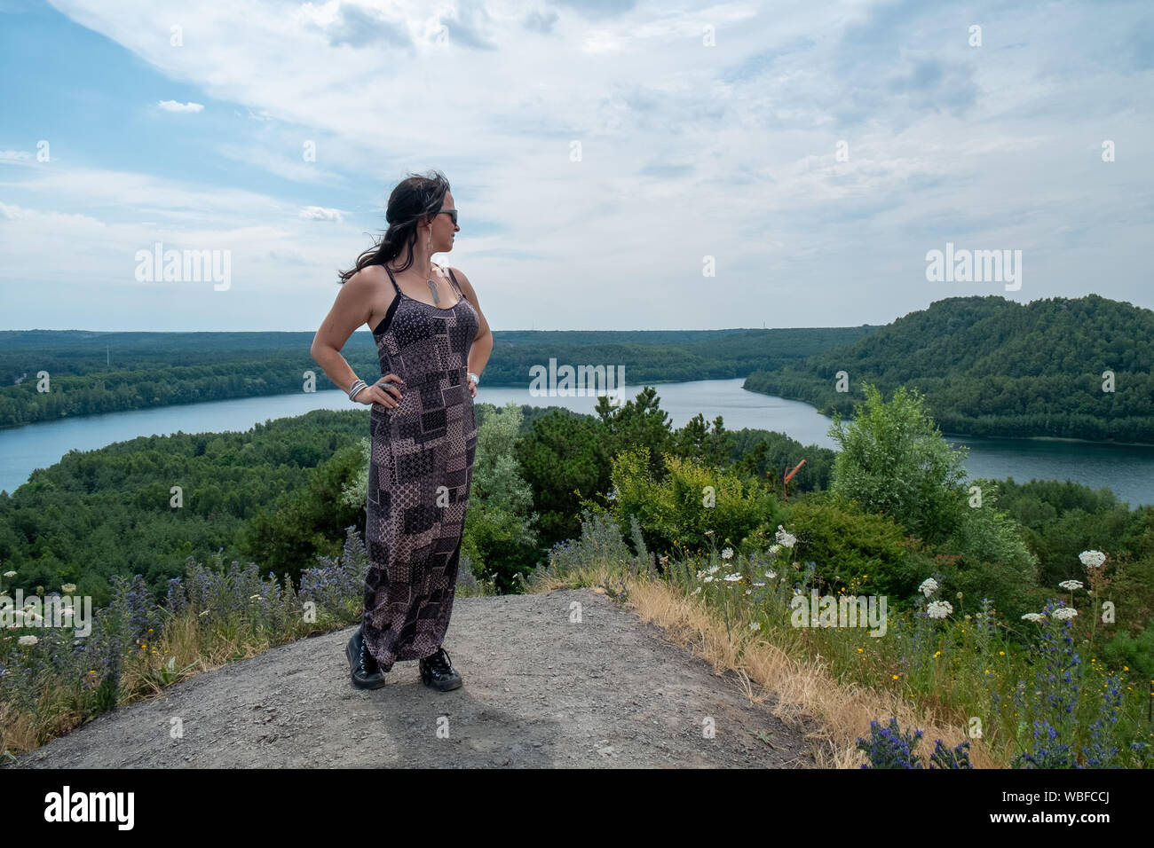 Mode femme de 30 à 40 ans à l'extérieur debout sur une colline avec une rivière qui coule à travers les bois sous un ciel bleu en arrière-plan Banque D'Images