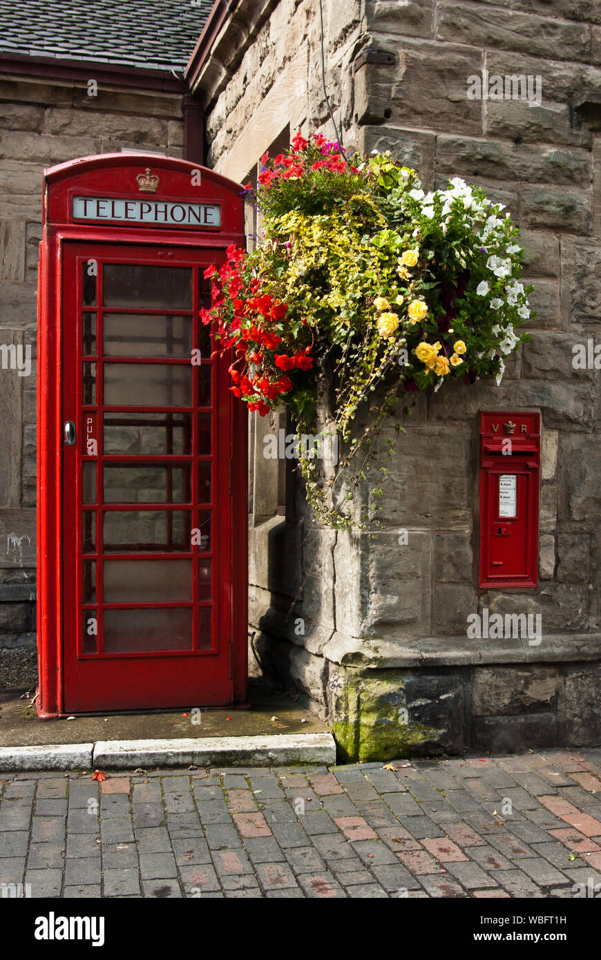 Boîte de téléphone rouge et boîte à côté d'un bâtiment en pierre avec des plantes suspendues Banque D'Images