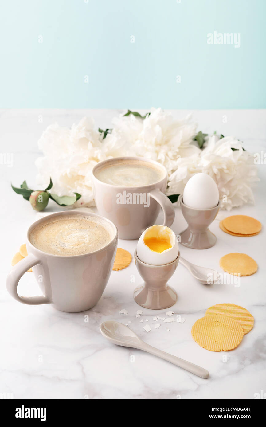 Des oeufs à la coque avec liquide jaune orange en céramique en cm, deux tasses de café avec des cuillères en céramique mince et croustillante et les croustilles de maïs sur fond de beau Banque D'Images