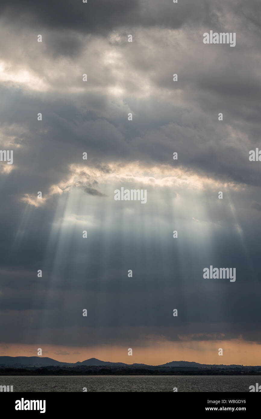 Du soleil au coucher du soleil, avec de sombres nuages en arrière-plan, un ciel orange, et du lac Trasimeno (Ombrie, Italie) ci-dessous Banque D'Images