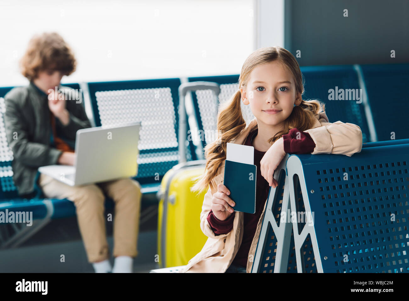 Selective focus on preteen kid holding passport et assis sur le siège bleu dans la salle d'attente Banque D'Images