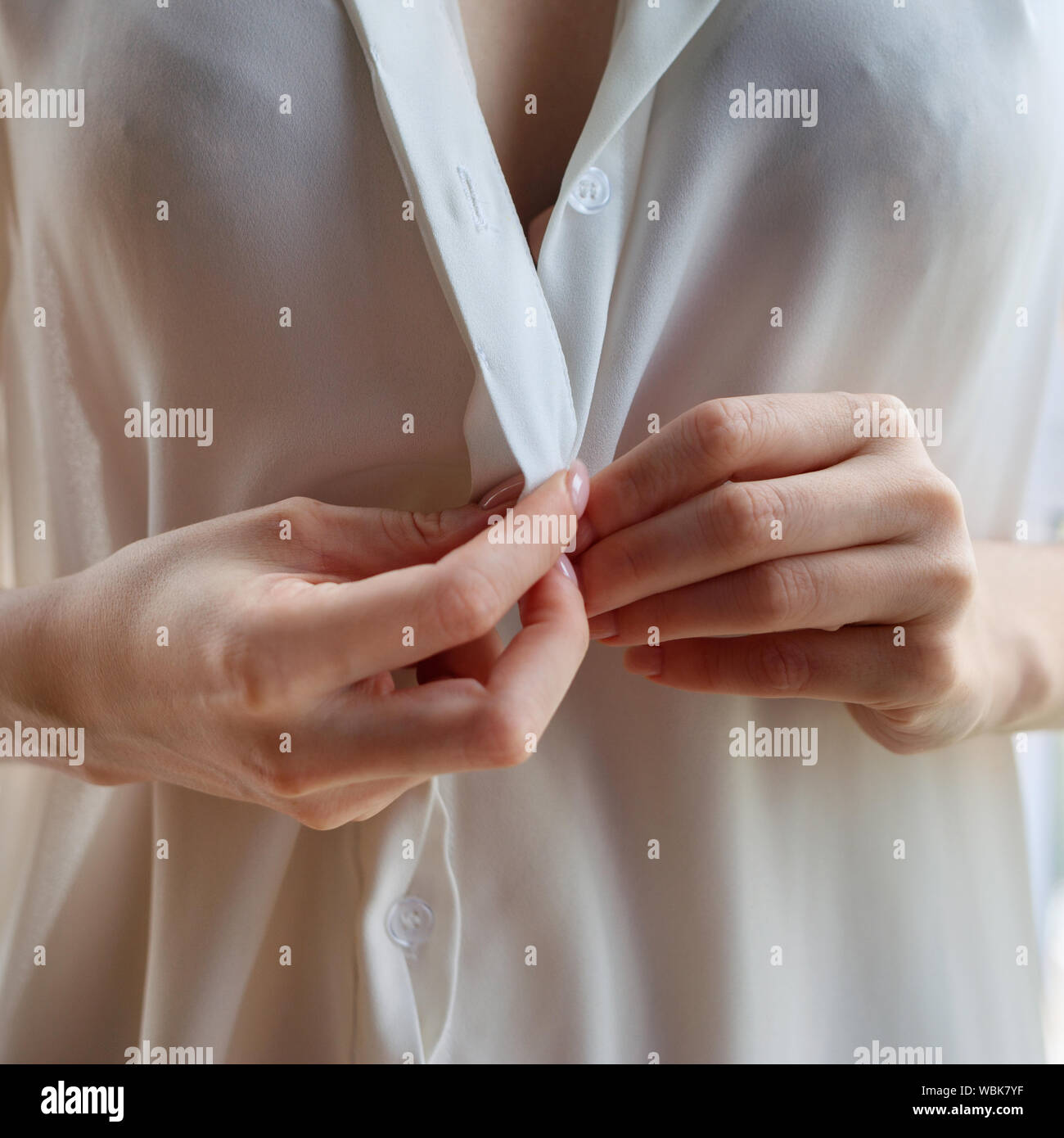 Méconnaissable femme unbuttoning chemisier blanc à la maison. Vue rapprochée sur les mains Banque D'Images