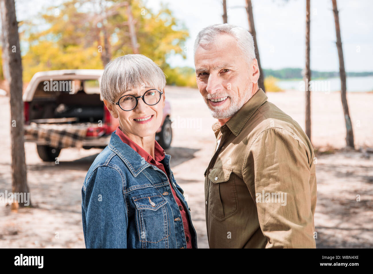 Happy senior couple looking at camera en forêt en journée ensoleillée Banque D'Images