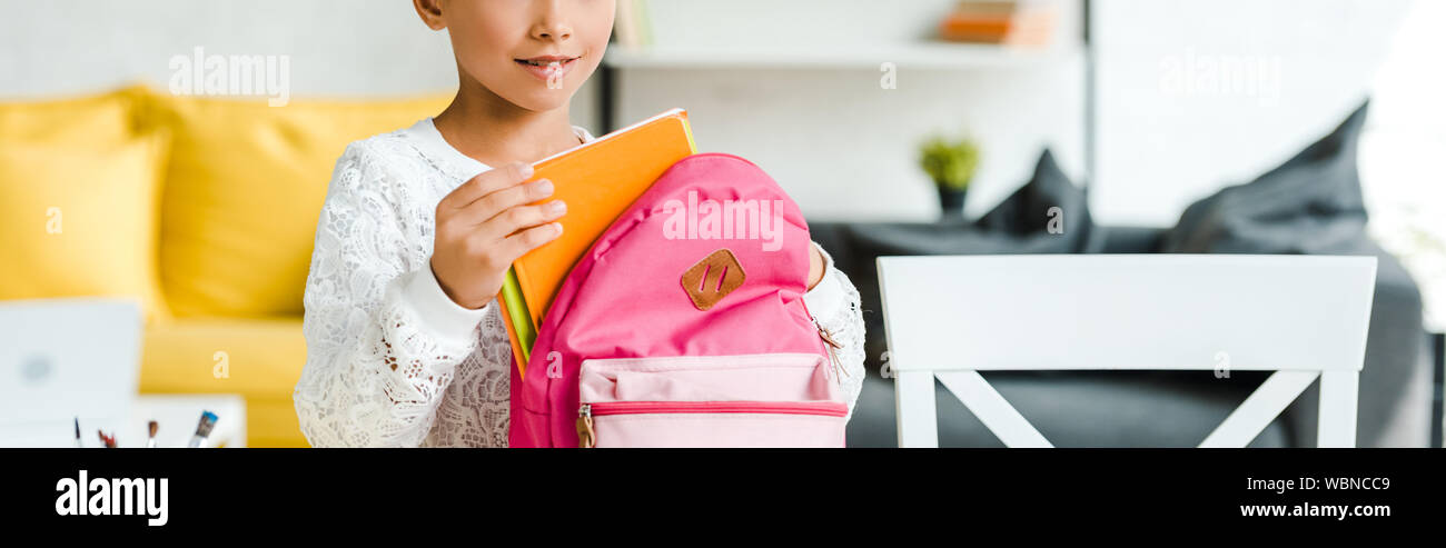 Vue panoramique tourné de Happy Child holding book près de sac à dos à la maison rose Banque D'Images