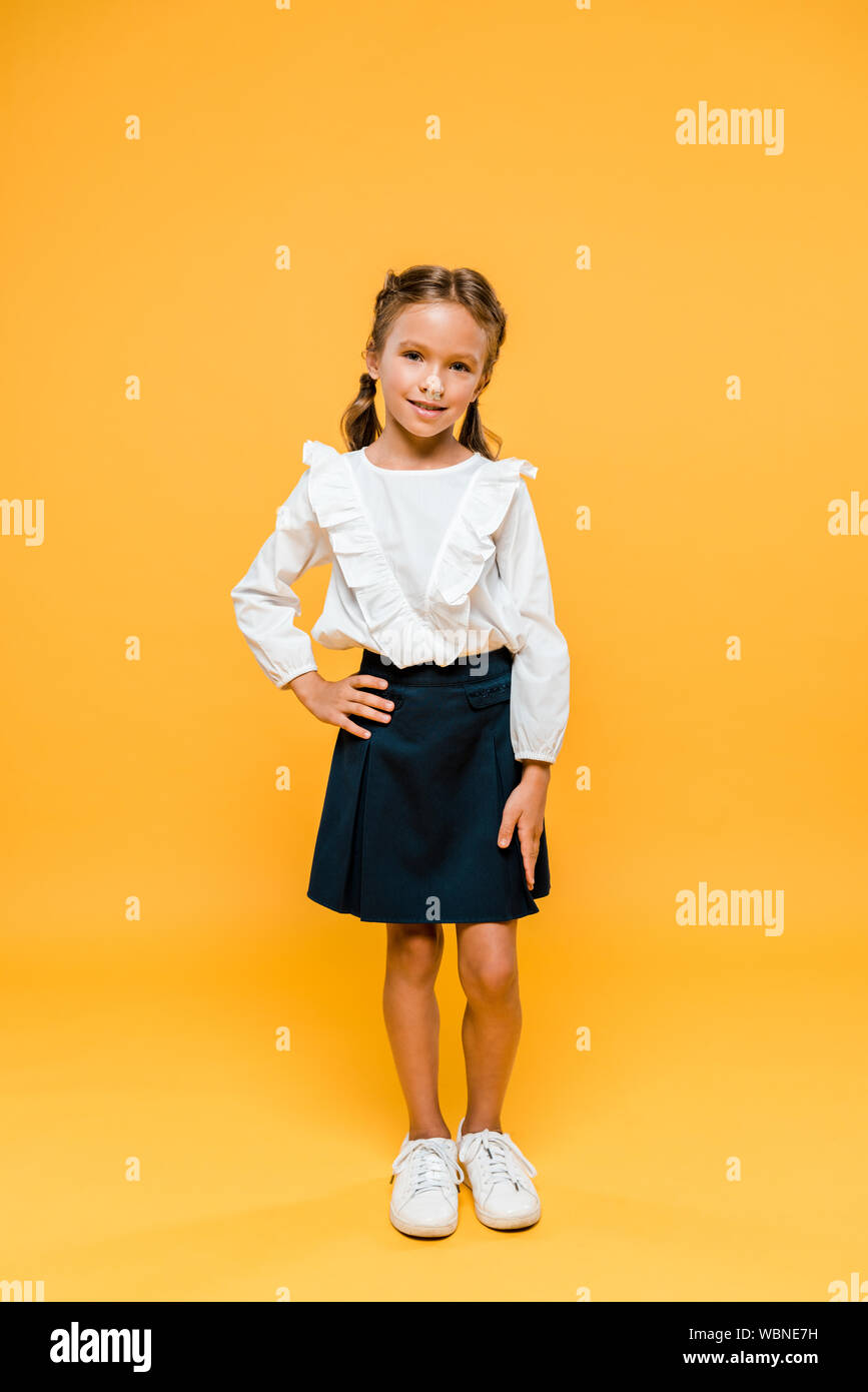 Heureux schoolkid standing with hand on hip sur orange Banque D'Images