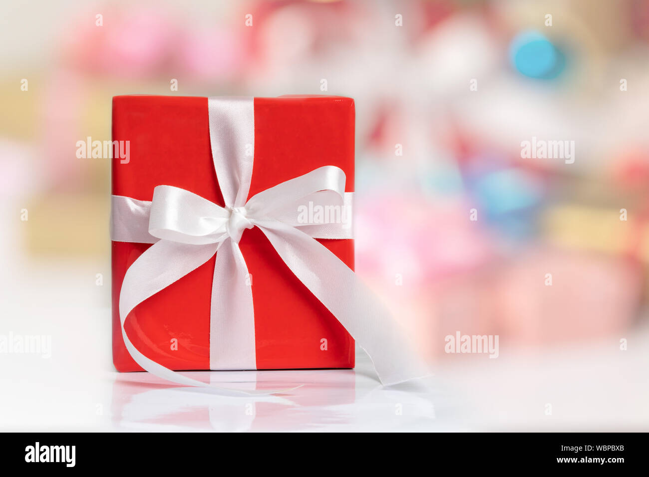 Une boîte cadeau rouge avec ruban blanc sur la table et fond flou pour tout concept de vacances avec copie espace. Des cadeaux surprises pour les occasions spéciales. Banque D'Images