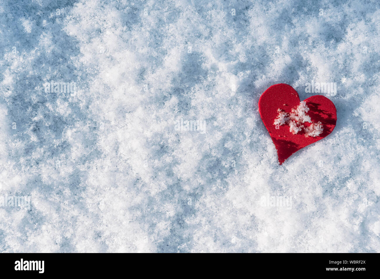 La neige fond et une forme de coeur rouge. Concept de la Saint Valentin. L'amour pour la saison d'hiver. Noël enneigé en toile de fond. Journée d'hiver ensoleillée. Banque D'Images