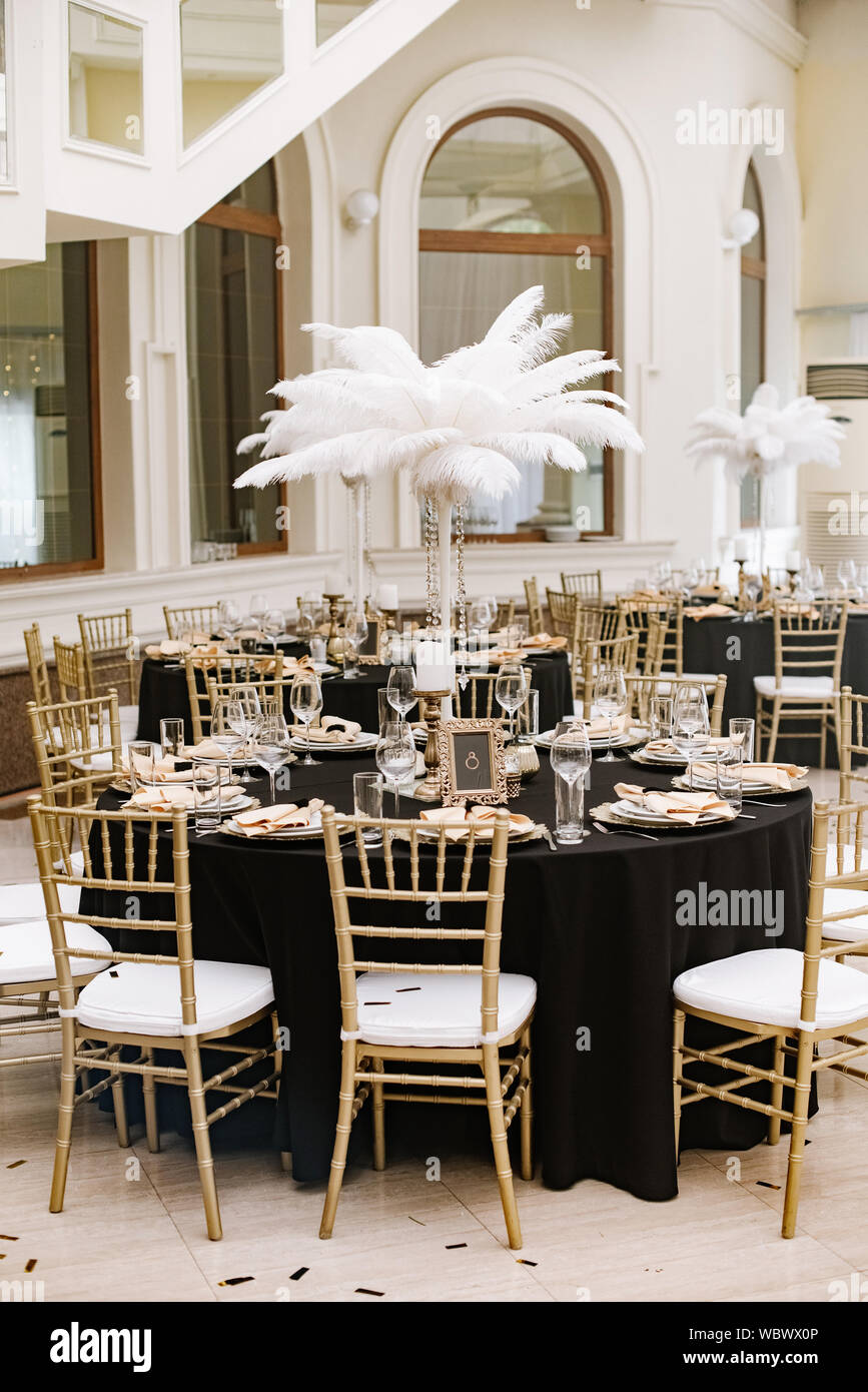Le design luxueux de la célébration du mariage dans le restaurant avec de grandes plumes blanches, chaises de style élégant et de détails dorés. Onglet noir Banque D'Images